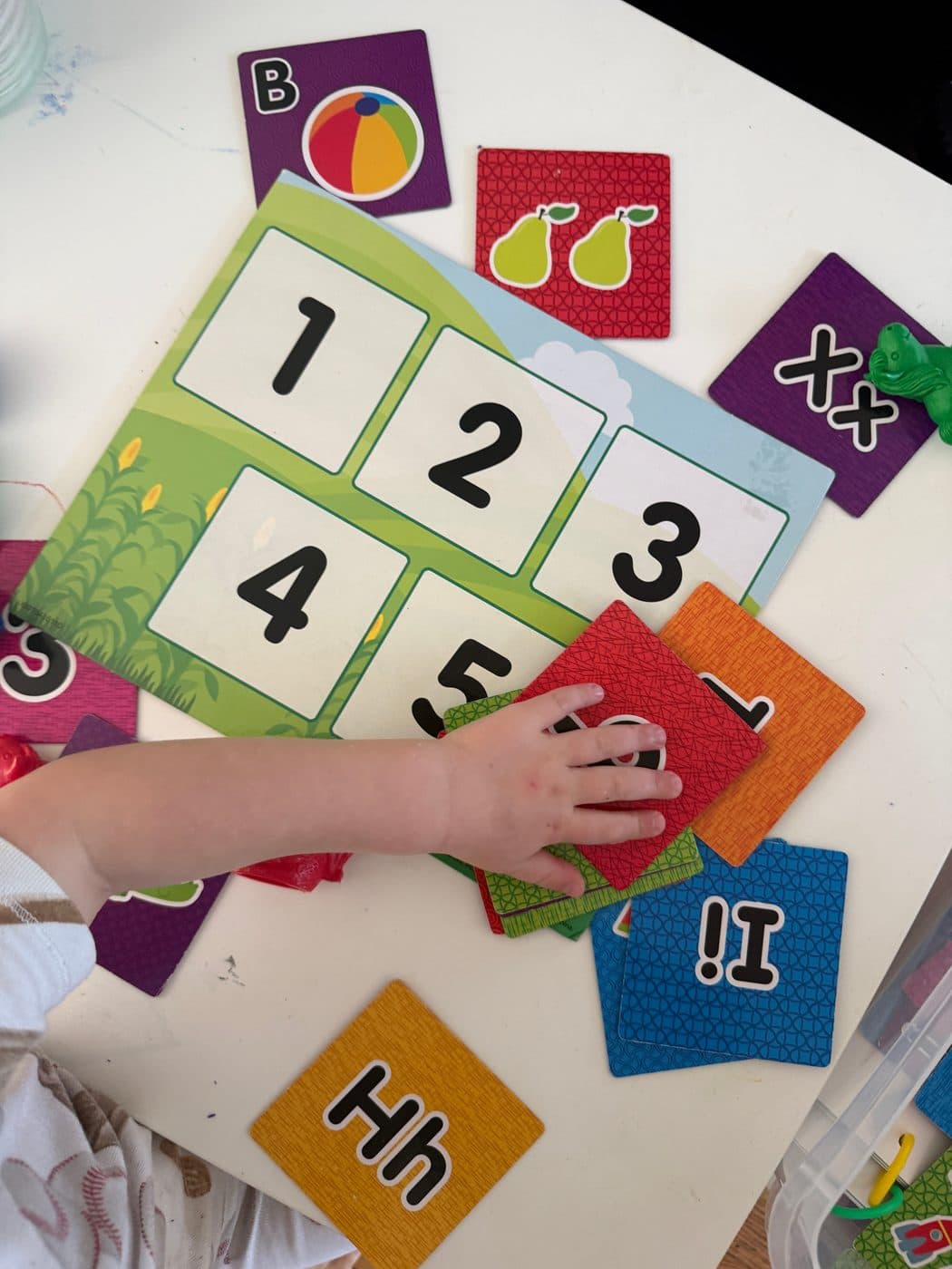 A child's hand arranging numbered cards and alphabet flash cards