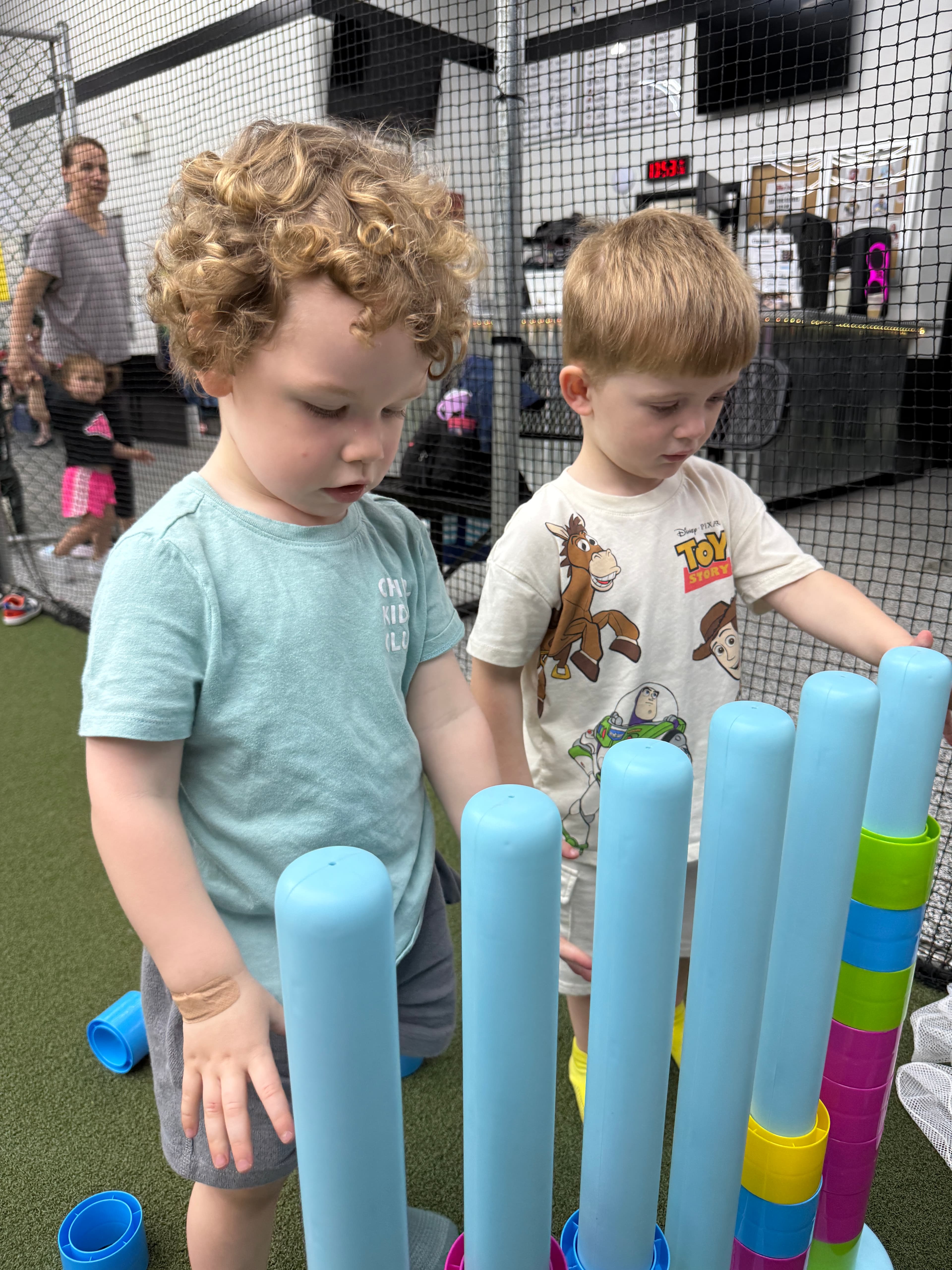 Two young boys working together to stack tall plastic tubes