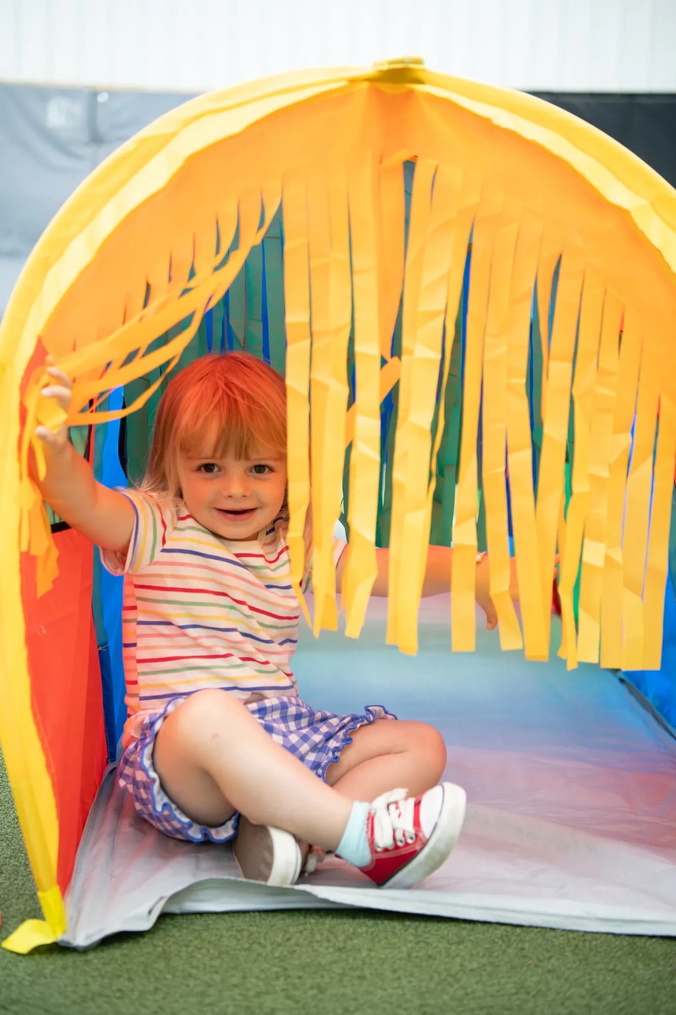 A young child playing inside a colorful streamer tunnel at a CHAMP Academy class