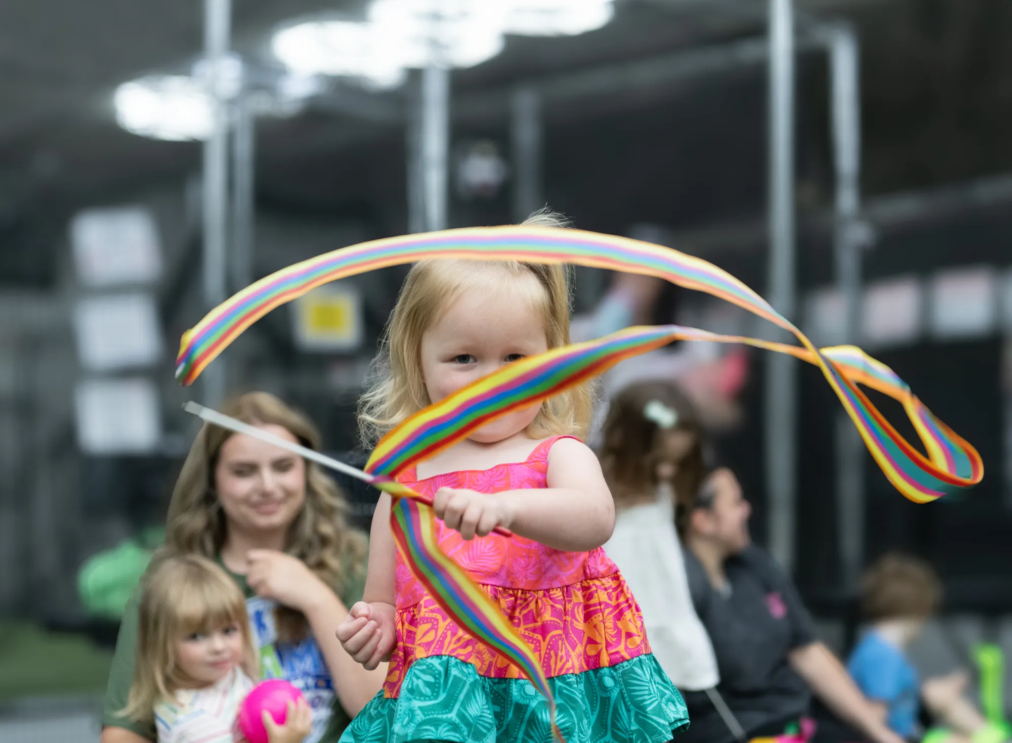 A toddler twirling a rainbow ribbon streamer during a CHAMP Academy movement class