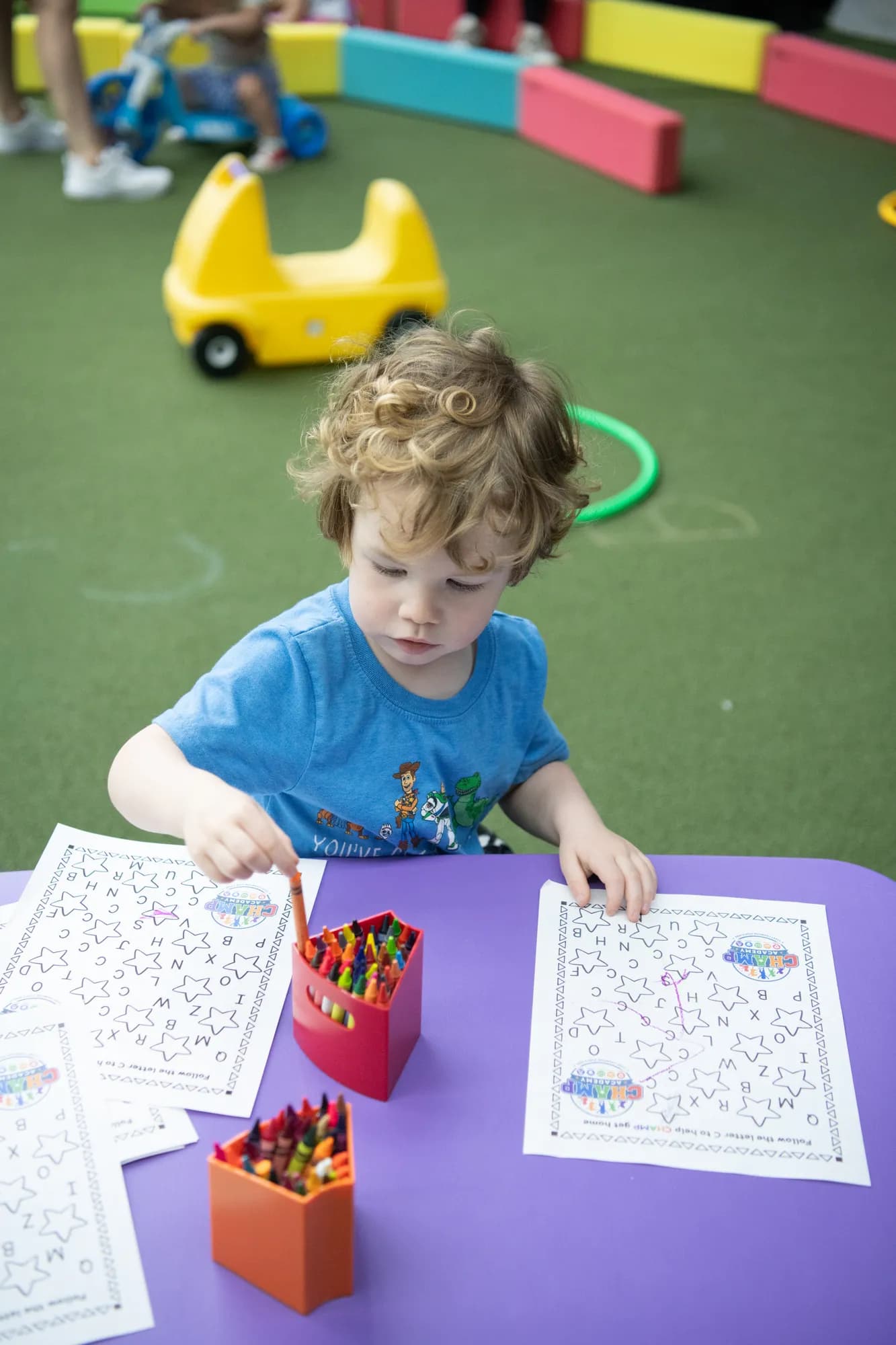 A child working on an alphabet activity sheet with crayons at a CHAMP Academy class