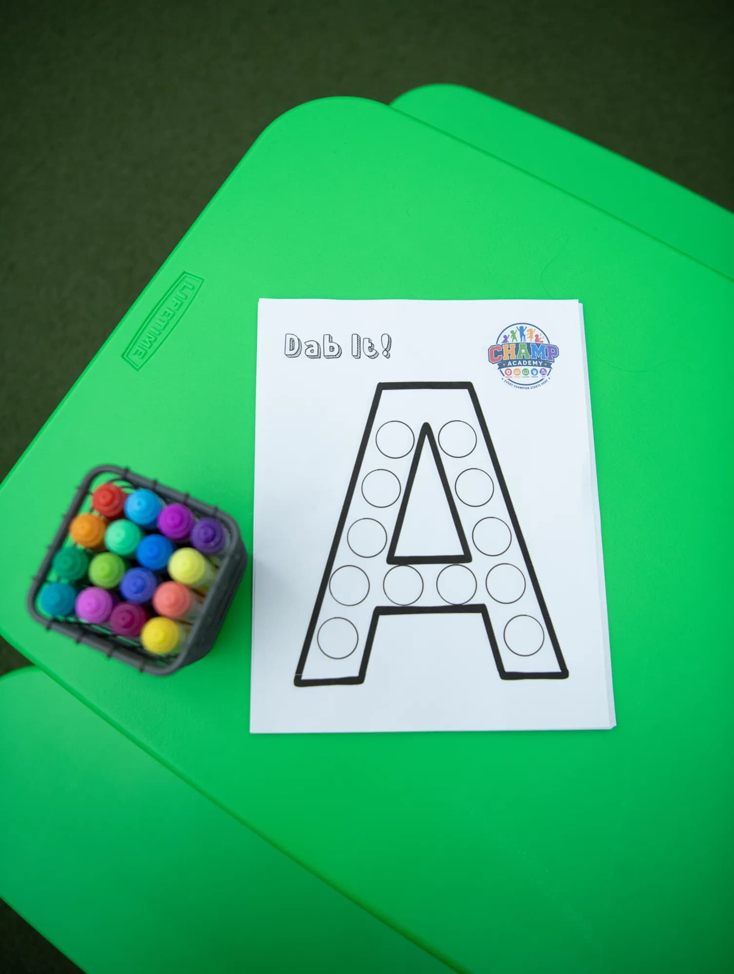 A dot-marker letter activity sheet with rainbow markers at a CHAMP Academy class
