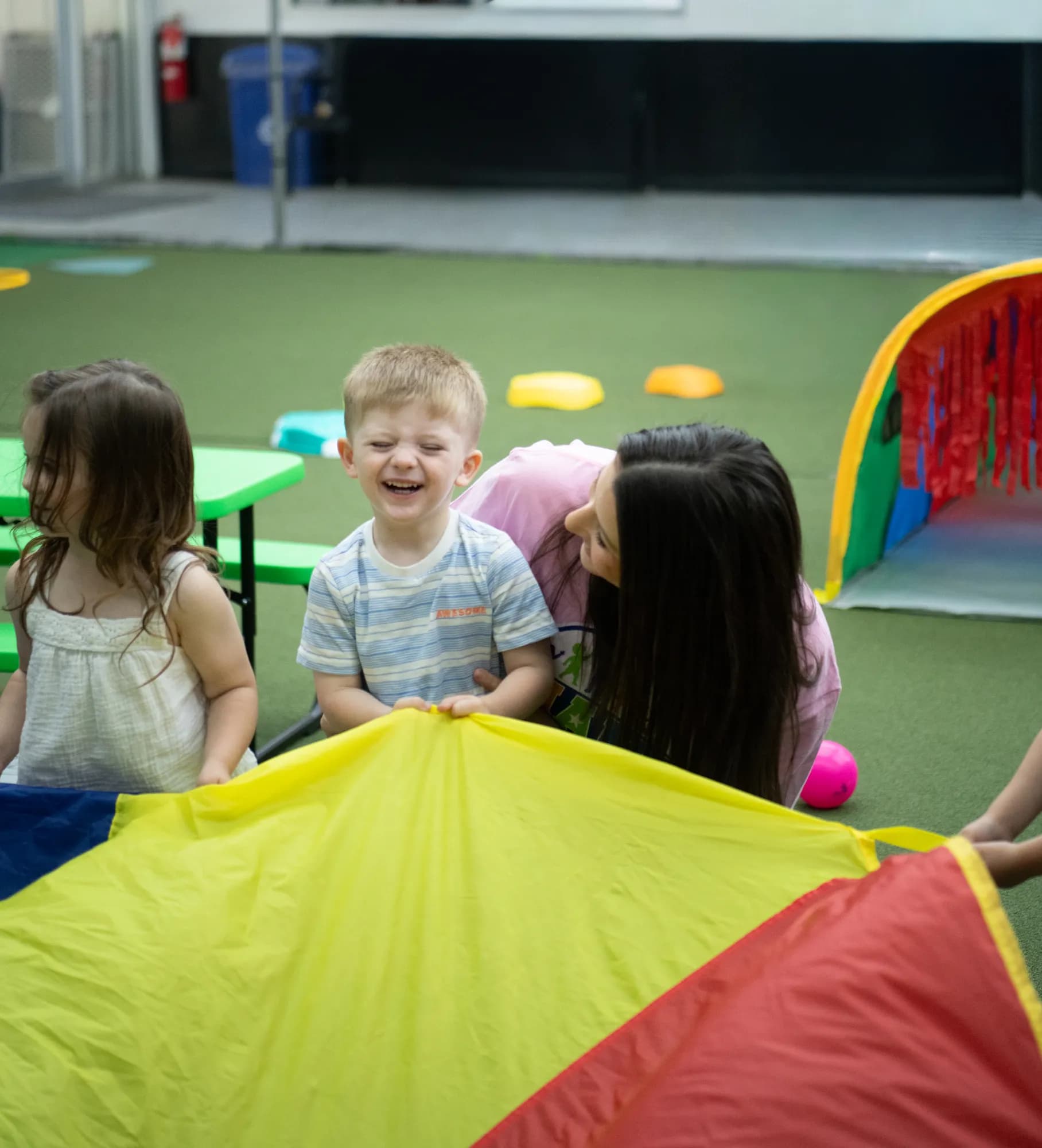A laughing child at a rainbow parachute during a CHAMP Academy class