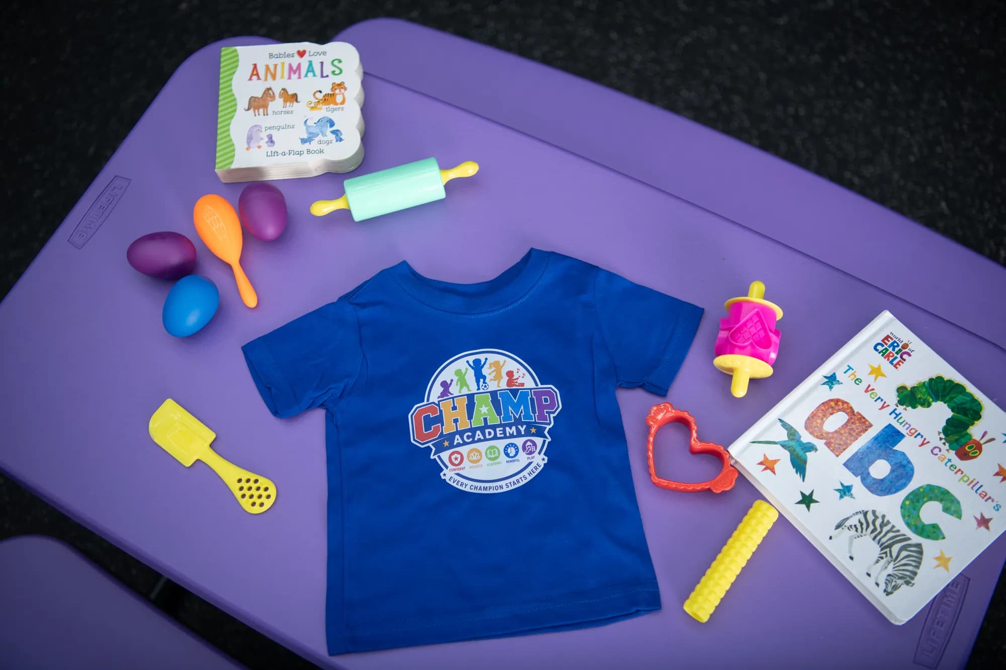 A CHAMP Academy t-shirt surrounded by classroom books and toys